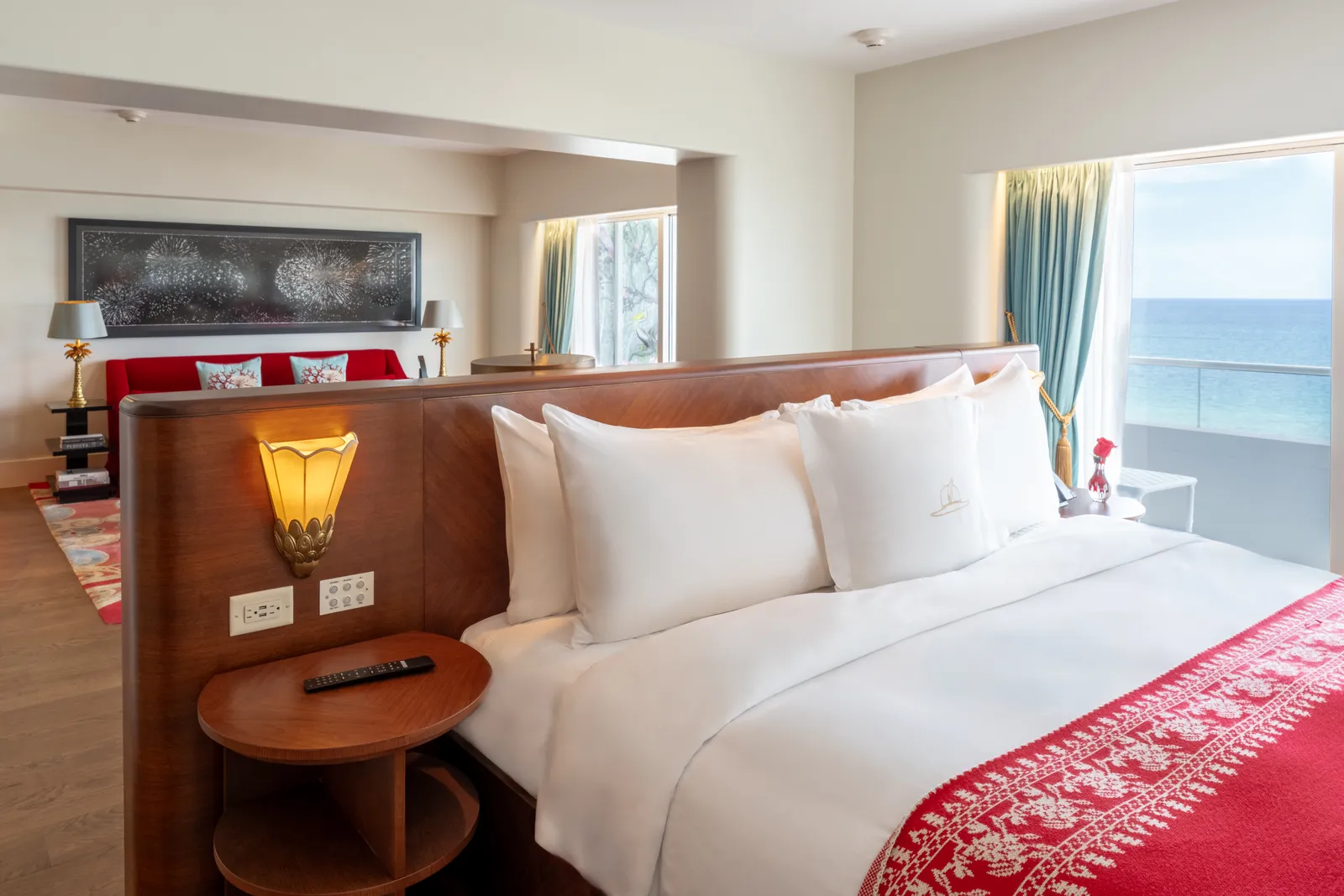 The Premier Oceanfront Corner Junior Suite: the bed with its red runner against the wooden divider and the ocean in the window.