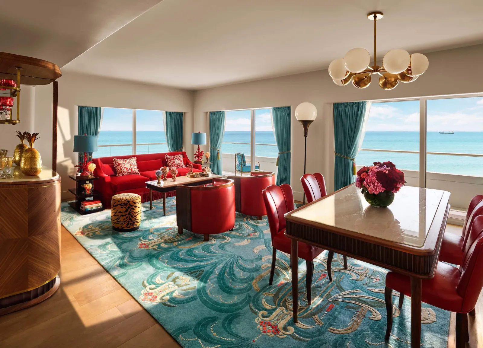 The Premier Oceanfront Corner Suite’s living room: the dining table with red chairs, the sofa and the ocean on 2 sides.
