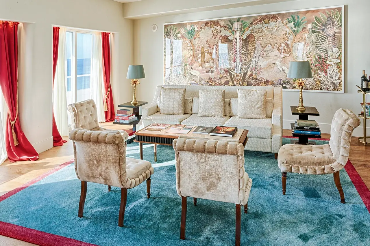 The 4-bedroom suite’s living room: patterned pale armchairs, a turquoise carpet and a large painting on the wall.