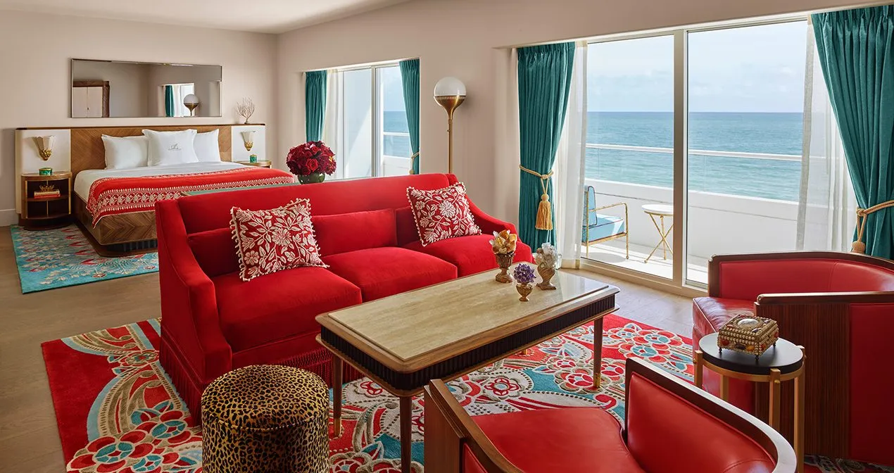 The Premier Oceanfront Junior Suite: the red sofa before the bed, turquoise curtains and the balcony over the ocean.