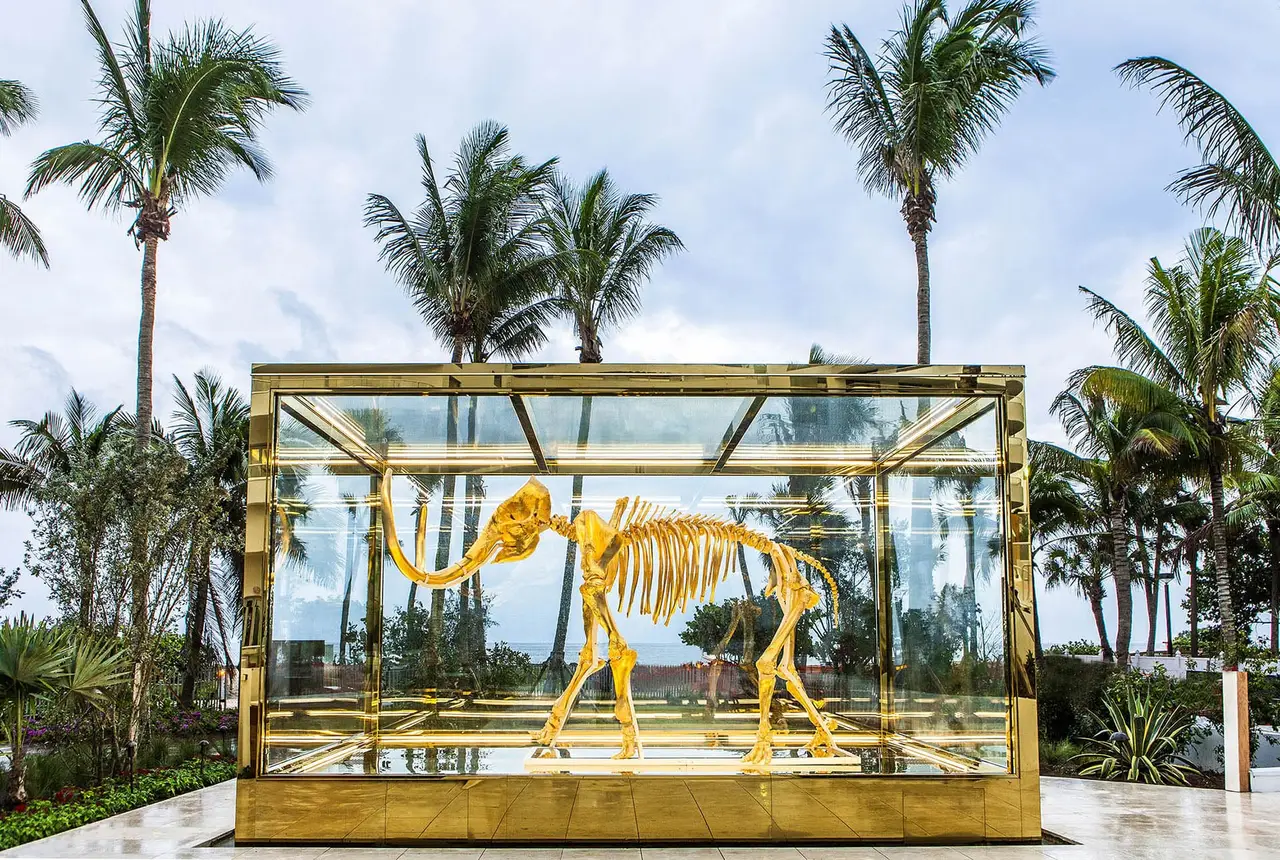 The gilded skeleton of a mammoth inside a glass and brass case, among the palms of the garden.