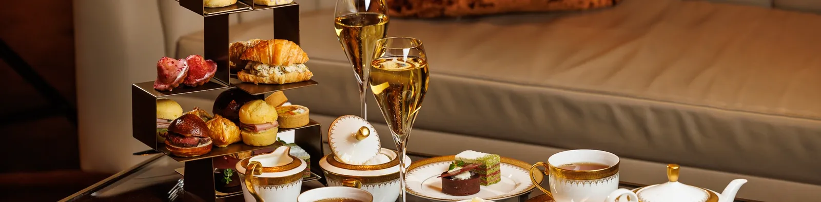 Alzate con dolci, sandwich e scones accanto a tazze e calici