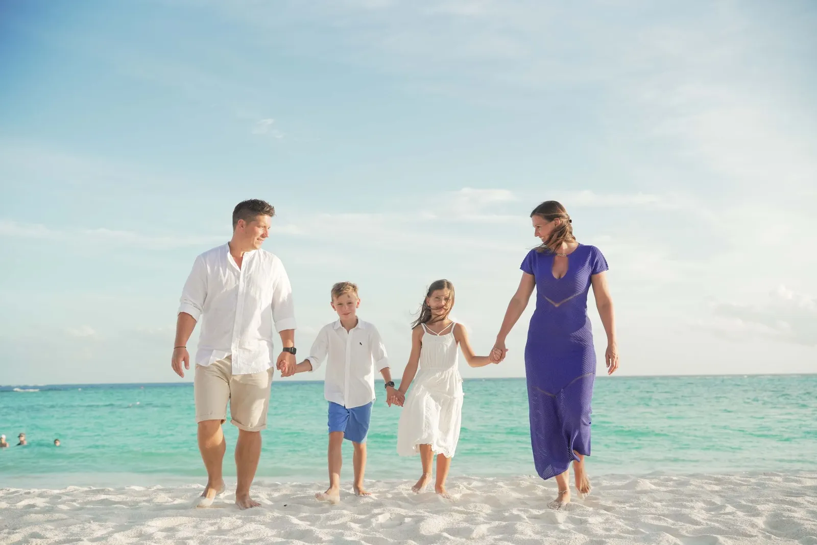 A family with 2 children walk hand in hand along the water’s edge.