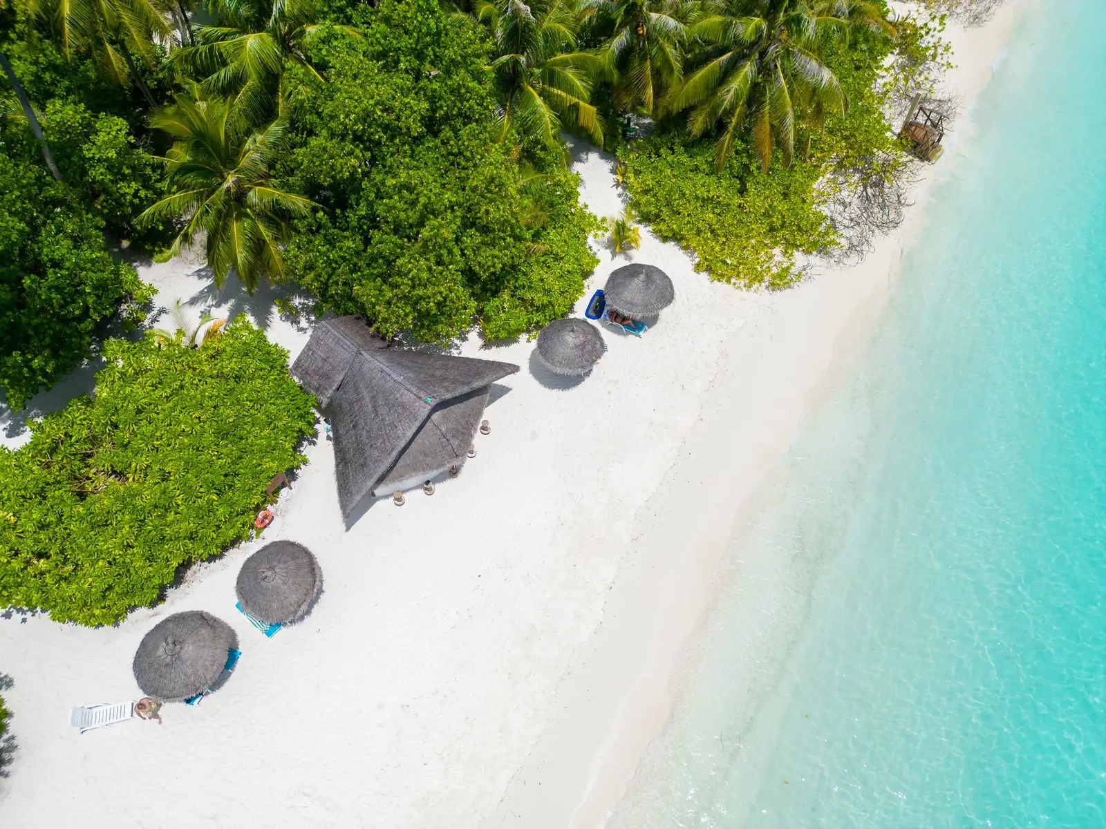 The beach from above: thatched parasols, a hut among the green and turquoise water along the shore.