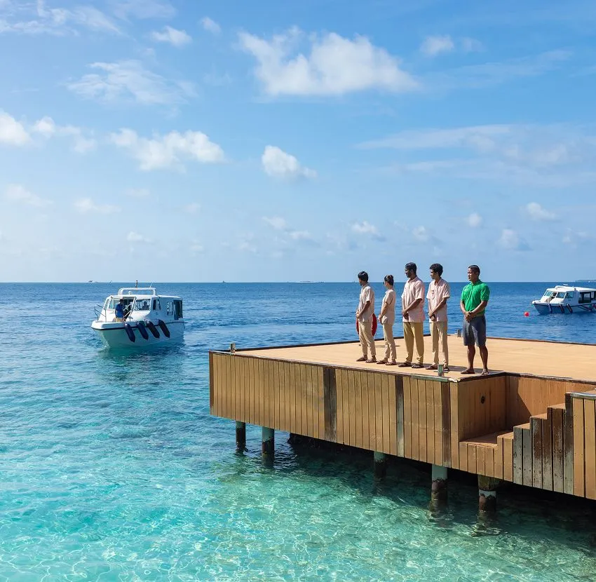 Staff lined up on the jetty platform as a speedboat comes in, above the clear water.