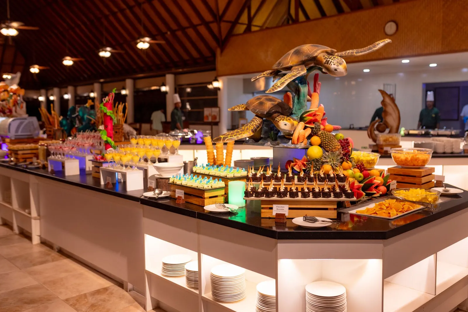 The Palm Grove buffet under the timber ceiling, with desserts, fruit and 2 carved turtles above the counter.