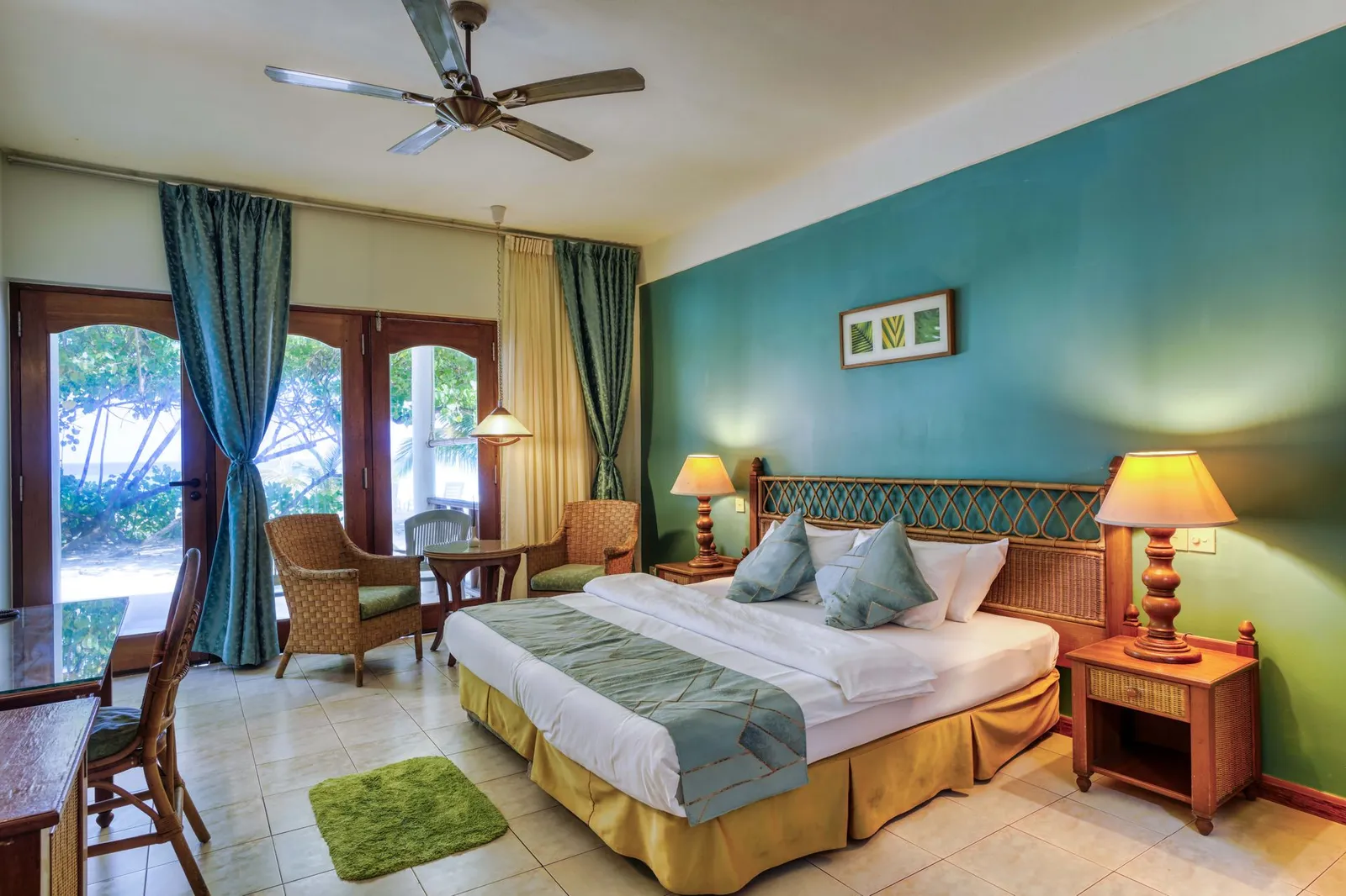 A ground-floor Deluxe Beach: the king bed, the blue wall, 2 armchairs and the glass doors onto the green.