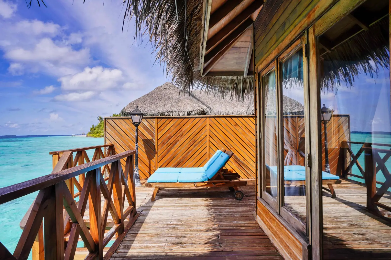 A Water Villa’s deck: the blue lounger, the timber railing and the turquoise lagoon under the thatched roof.