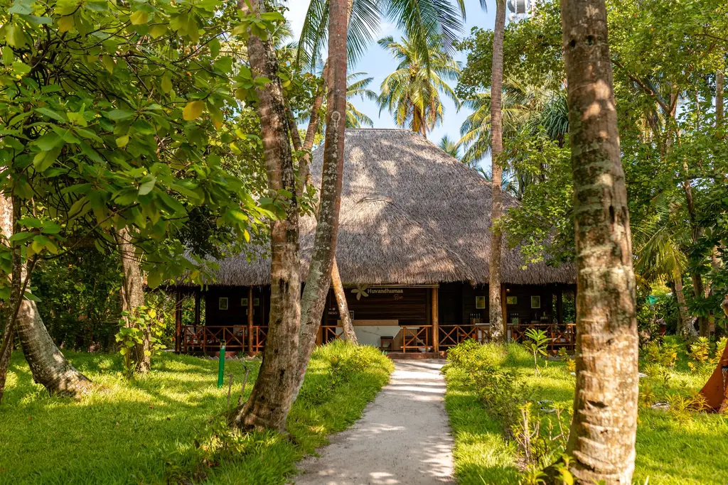 The spa pavilion with its thatched roof at the end of a path through the palms and the lawn.