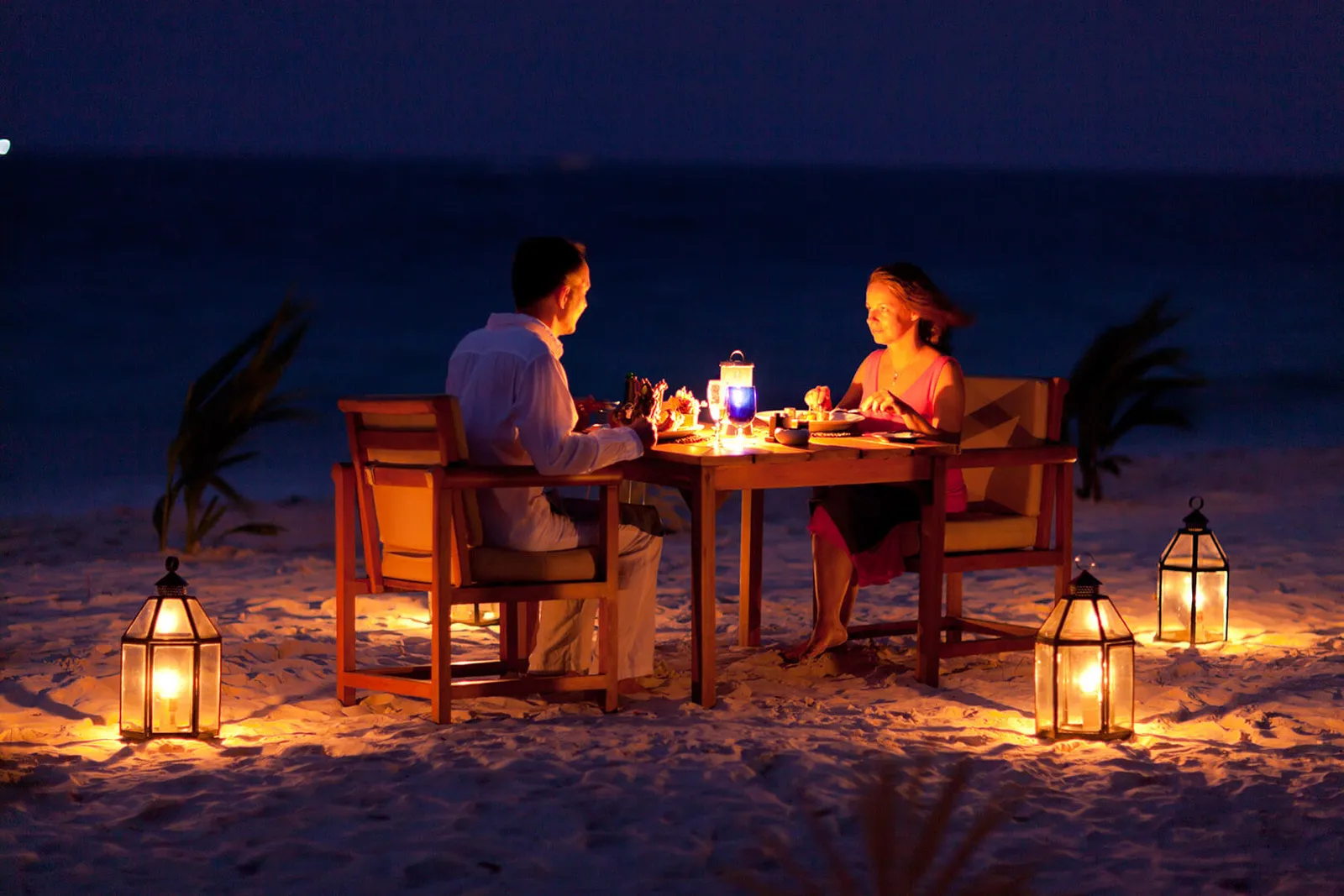 Dinner for 2 on the beach at night, the table laid among lanterns lit on the sand.
