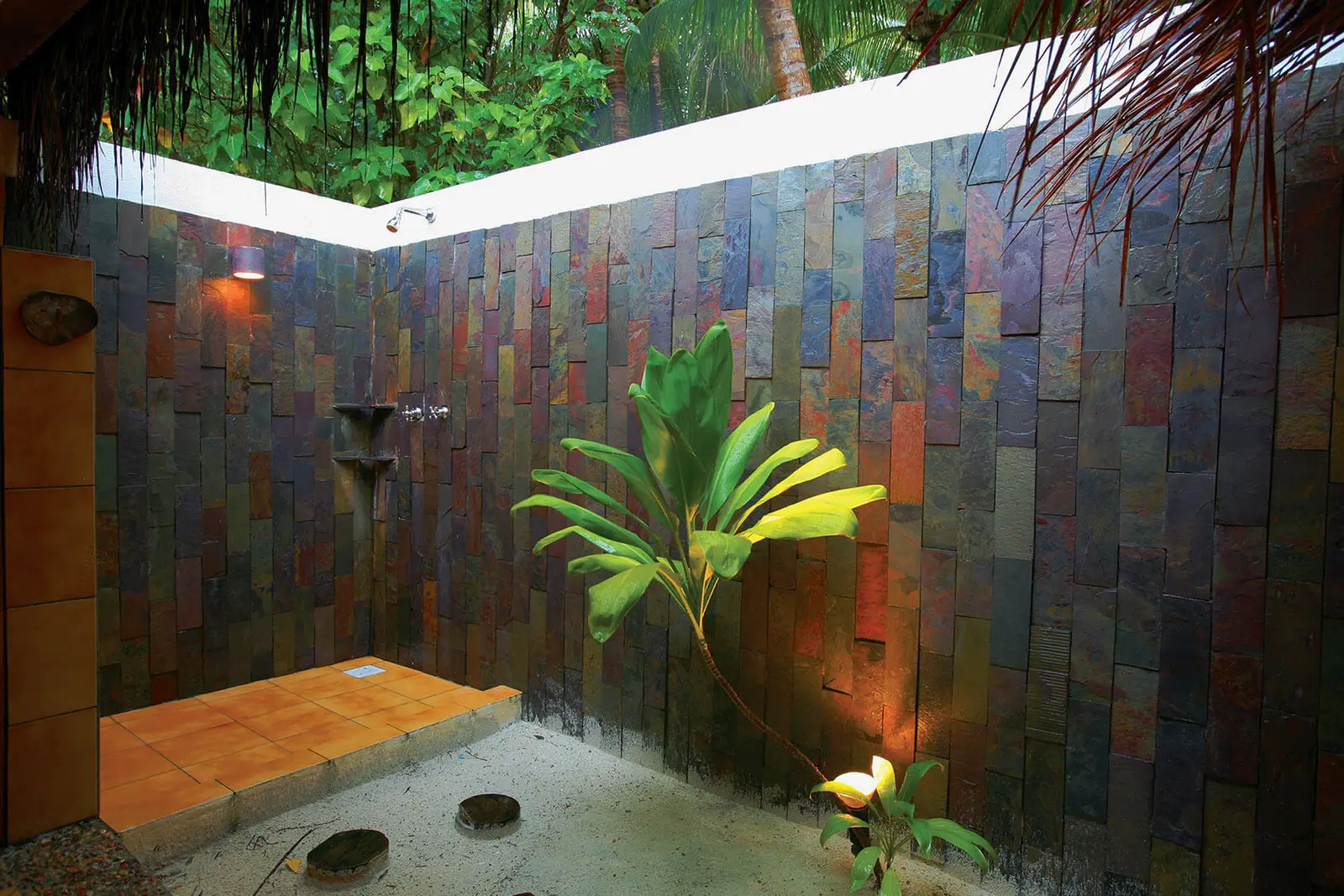 A Superior Villa’s open-air shower, between walls of dark stone, with a plant and the sky above.