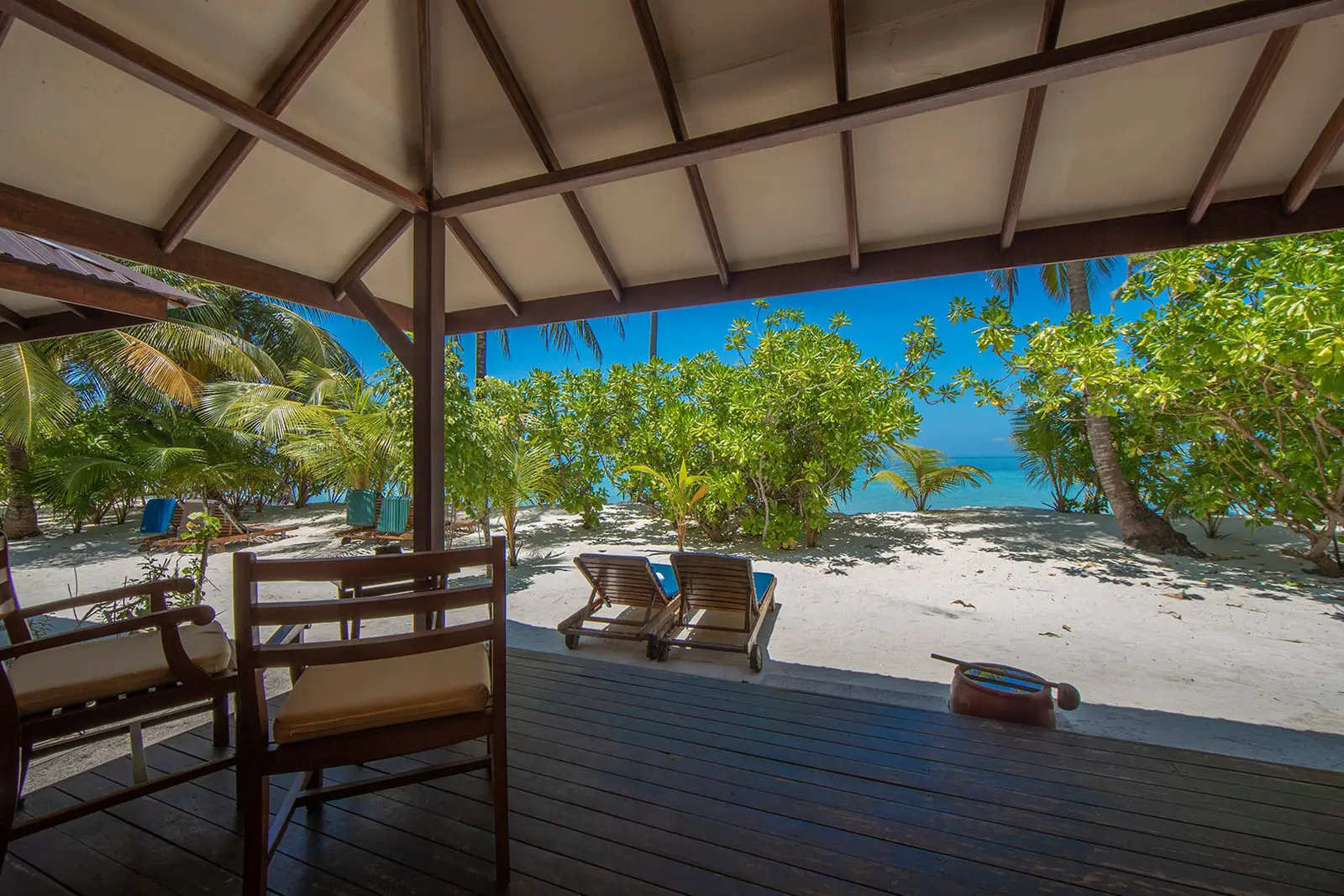A Superior Villa’s wooden veranda, with its table and chairs, the beach, the loungers and the sea ahead.