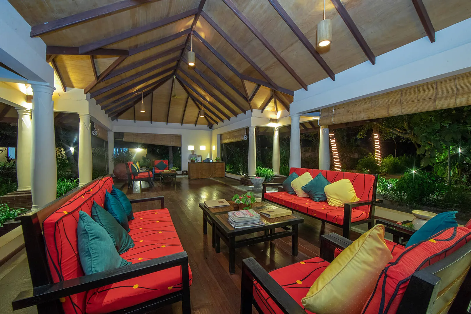 The spa lounge under its timber roof, with red sofas and bright cushions, open to the garden.