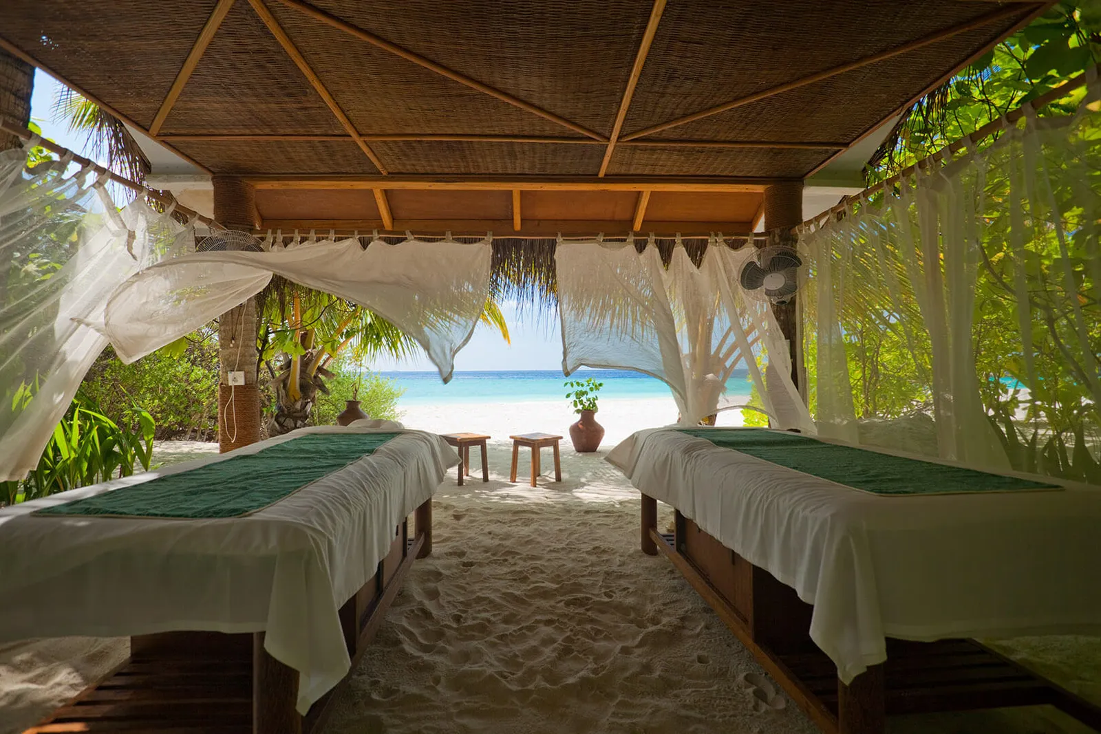2 massage beds under the spa’s open pavilion, between white curtains, with the beach and the sea beyond.