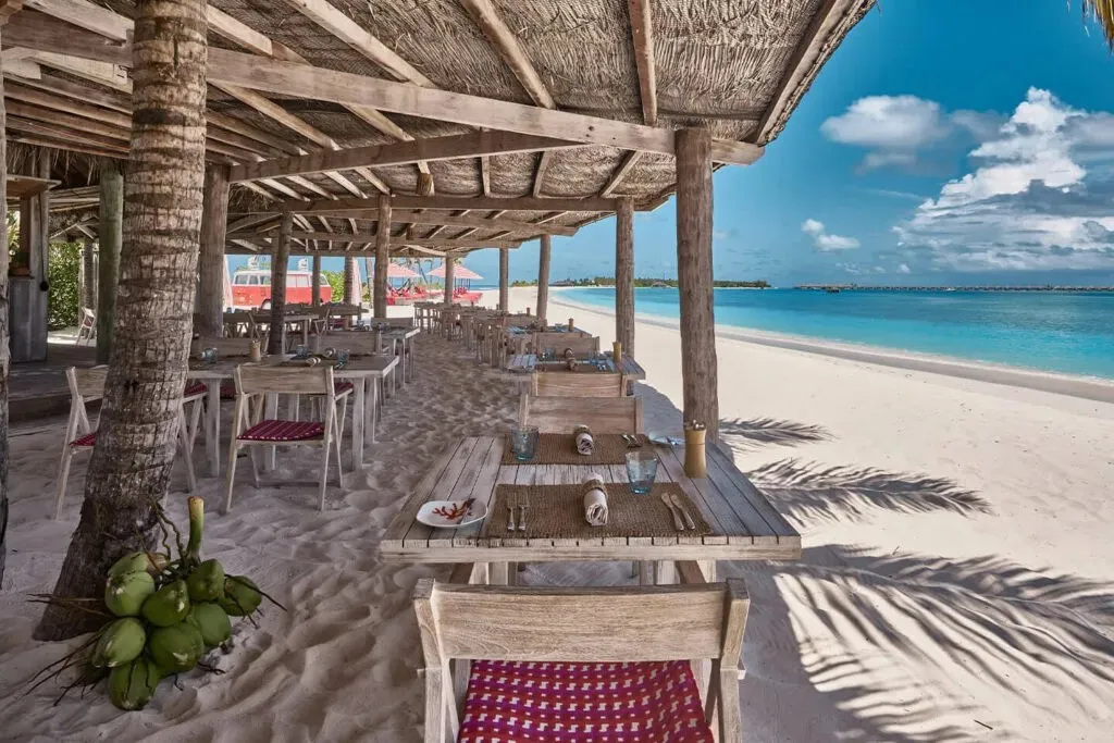 The Crab Shack’s tables in the sand under the thatched roof, facing the beach