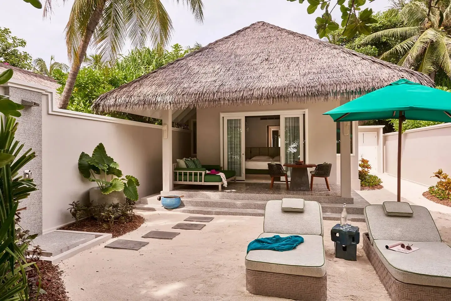 A Beach Villa under its thatched roof, loungers in the courtyard and a green umbrella