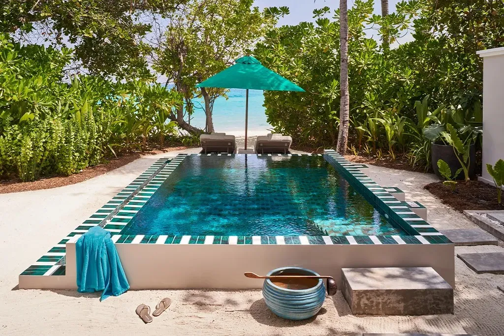 The Interconnecting Three-Bedroom Beach Pool Villa’s pool among the plants, with a green umbrella