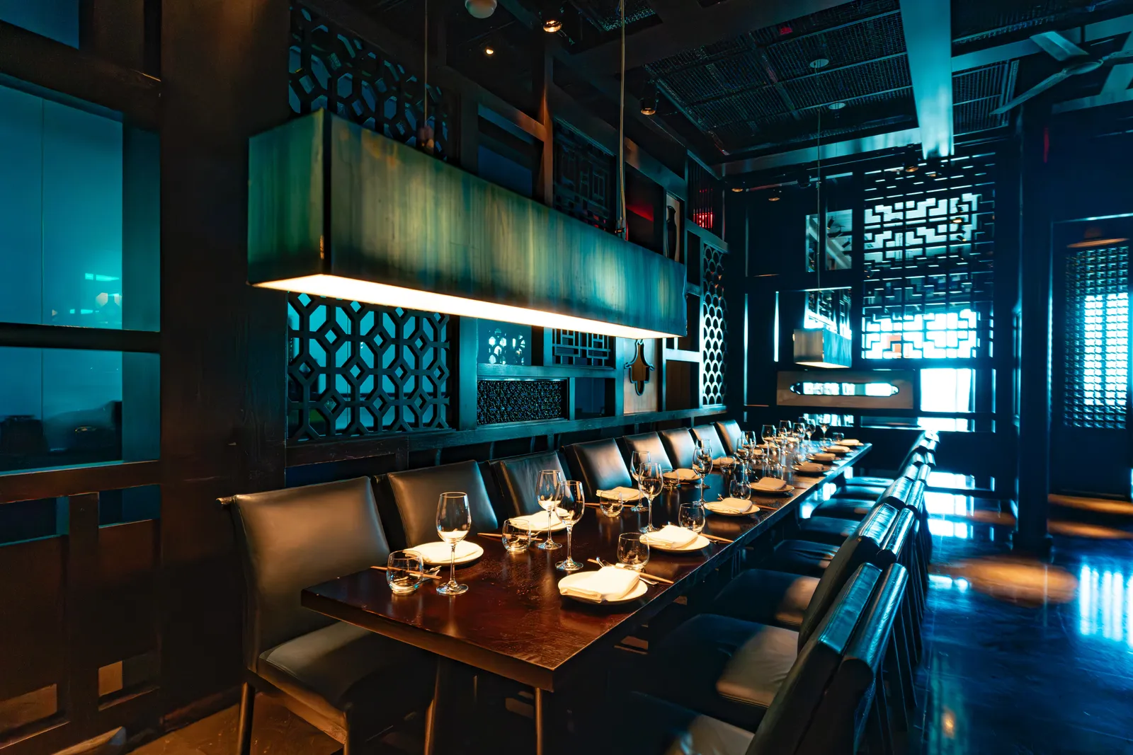 Hakkasan’s dining room: a long laid table under a rectangular lantern, between carved wooden screens in blue light.