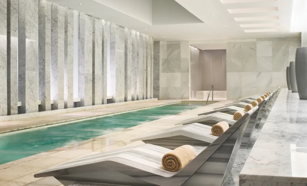 Lapis Spa’s long, narrow mineral pool, with a row of stone loungers and rolled towels along its edge and marble walls.
