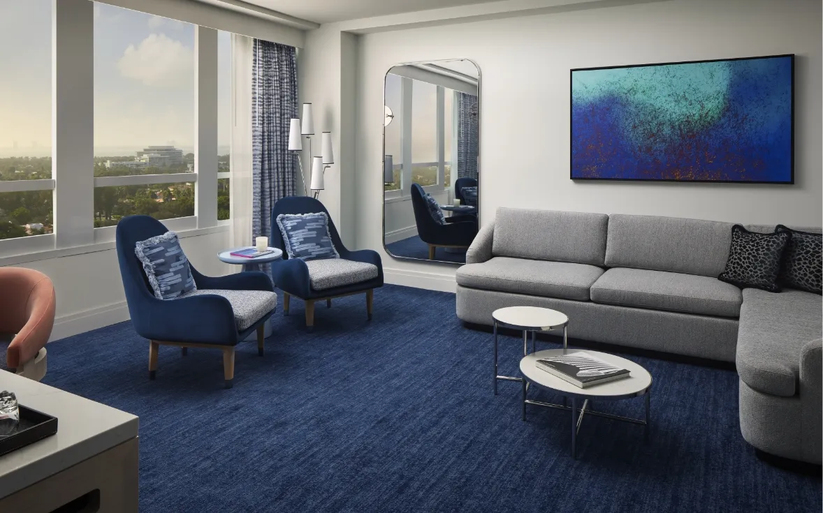 The sitting area of a Bay View Junior Suite: a grey corner sofa, 2 blue armchairs, a blue and green painting and the windows over the city.