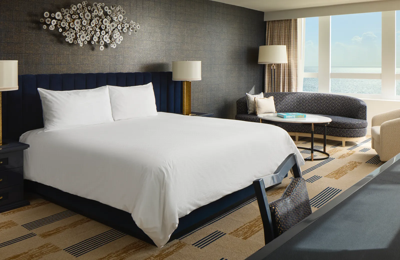 A bedroom of the Bleau Moon Suite: the king bed with its blue headboard, a curved sofa and the windows along the coast.