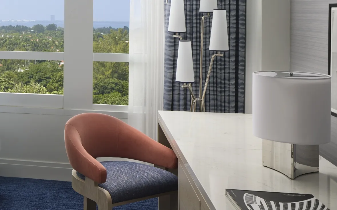 The desk with its coral chair and lamp, beside the windows over the trees and the bay.