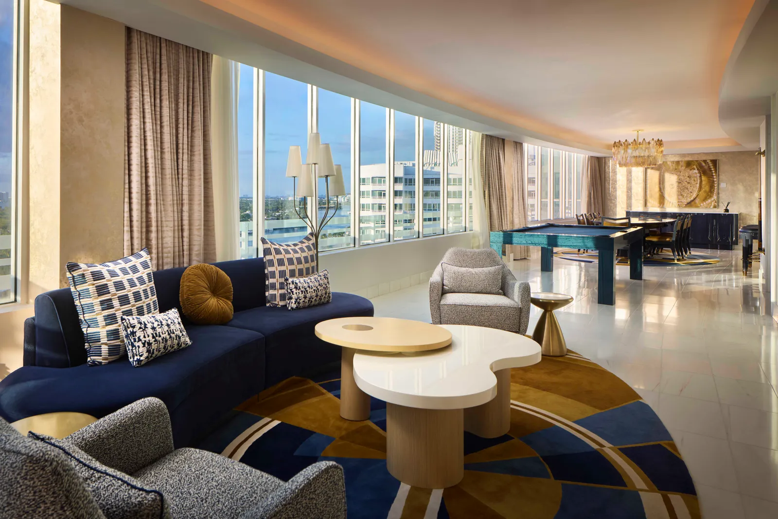 The La Baie Presidential Suite’s living room: blue sofas on a rug of blue and gold circles, a long window wall and the billiards table at the far end.