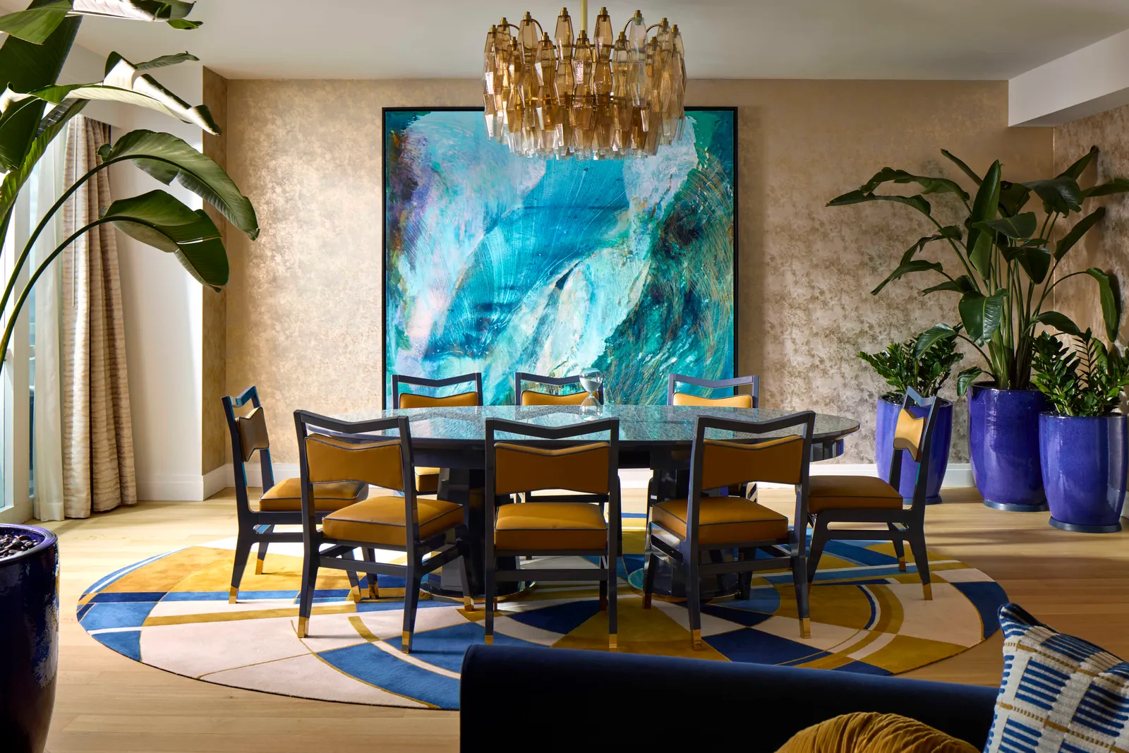 The Le Sable Presidential Suite’s dining room: a table with mustard chairs under a gilt chandelier, a large blue painting and plants.