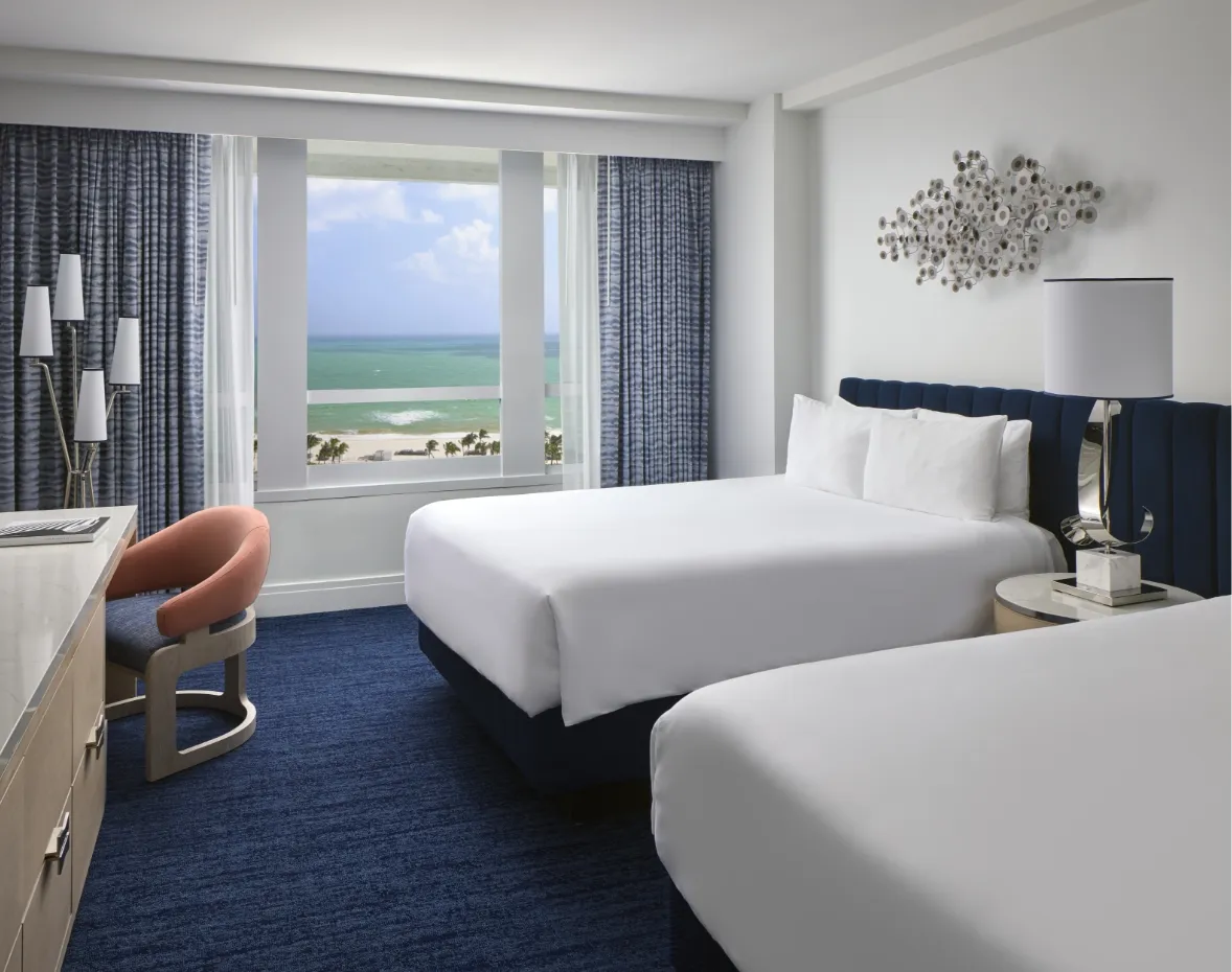 An Ocean View room with 2 queen beds, blue carpet and the window onto the beach and the ocean.