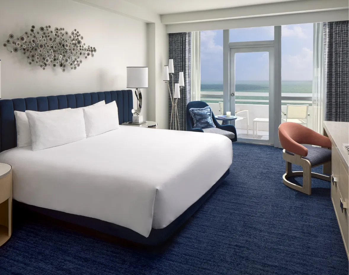 An Oceanfront room with a king bed and blue headboard, armchairs and the door to the balcony facing the ocean.