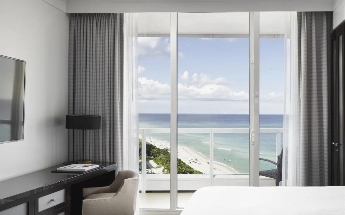 From the bedroom of a Sorrento tower suite: the dark desk, grey curtains and the glass door to the balcony, with the beach and ocean below.