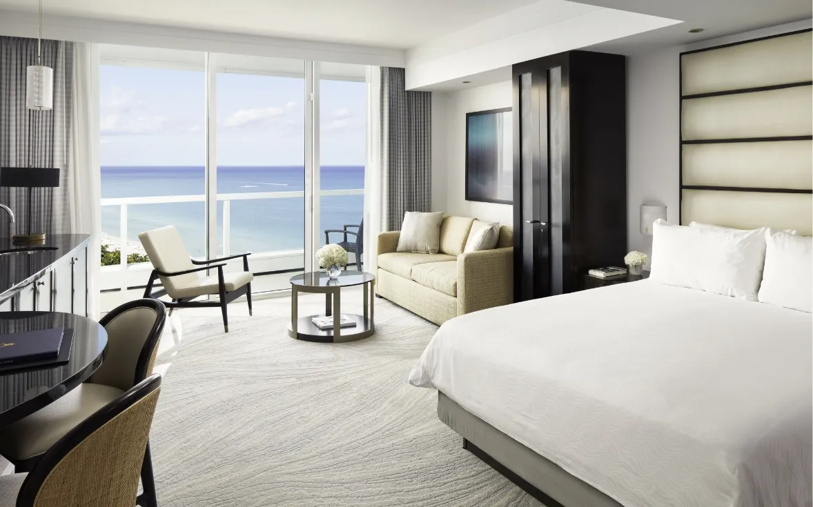 A Sorrento Oceanfront Junior Suite, with its tall pale headboard, the sofa and the sea beyond the glass.
