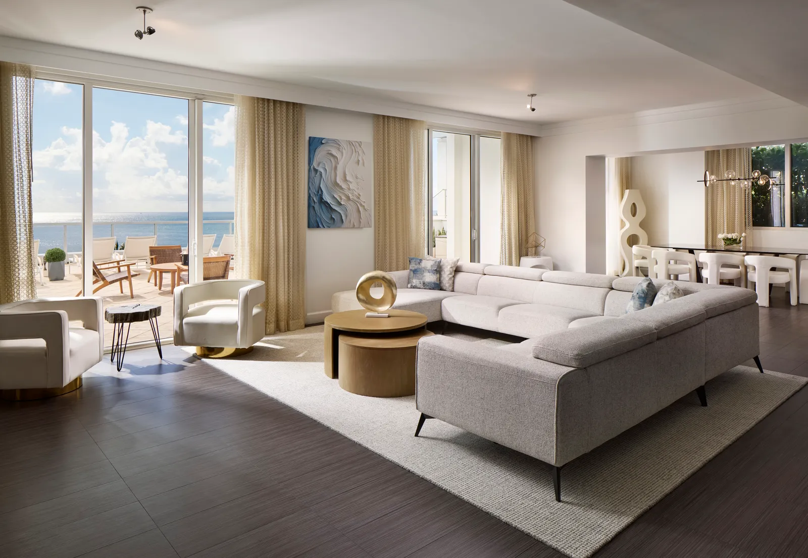 The Sorrento Penthouse’s living room: a large pale corner sofa, dark floor, the dining area and the glass doors onto the terrace and the sea.