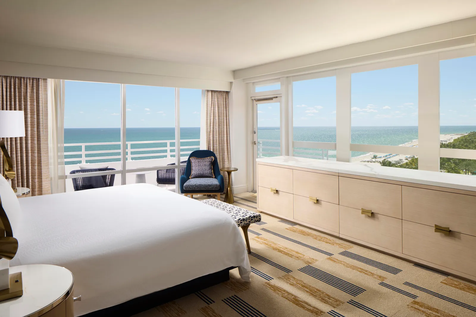 A bedroom of the Versailles Oceanfront Two Bedroom Suite: the bed, a long pale sideboard and corner windows over the beach.
