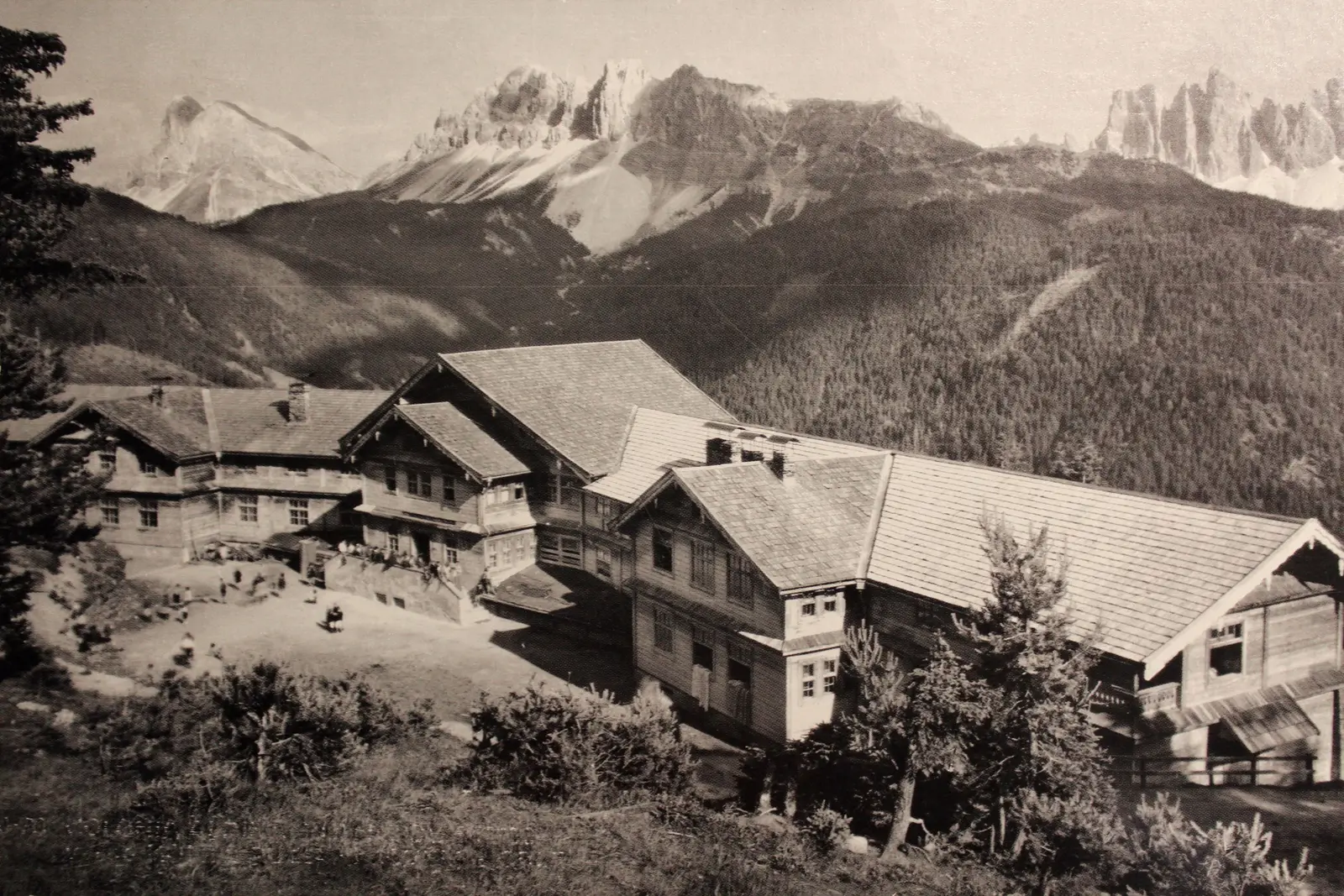 A black-and-white archive photograph: the wooden buildings of Palmschoß on the slope, with the Dolomites behind.