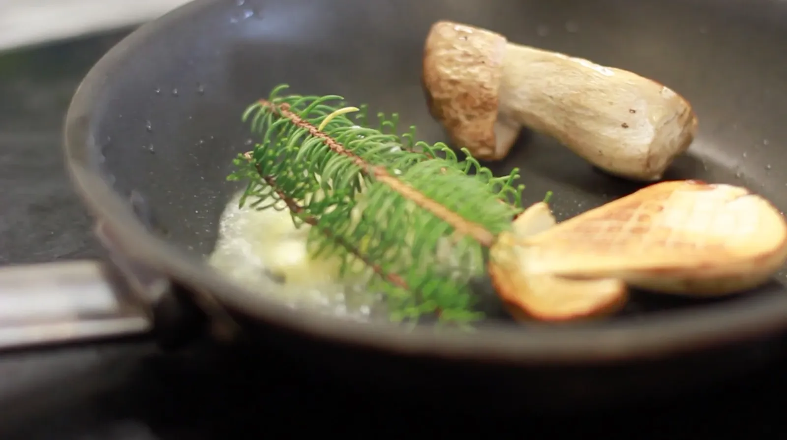 2 halved porcini in an iron pan, with a sprig of fir and melting butter.