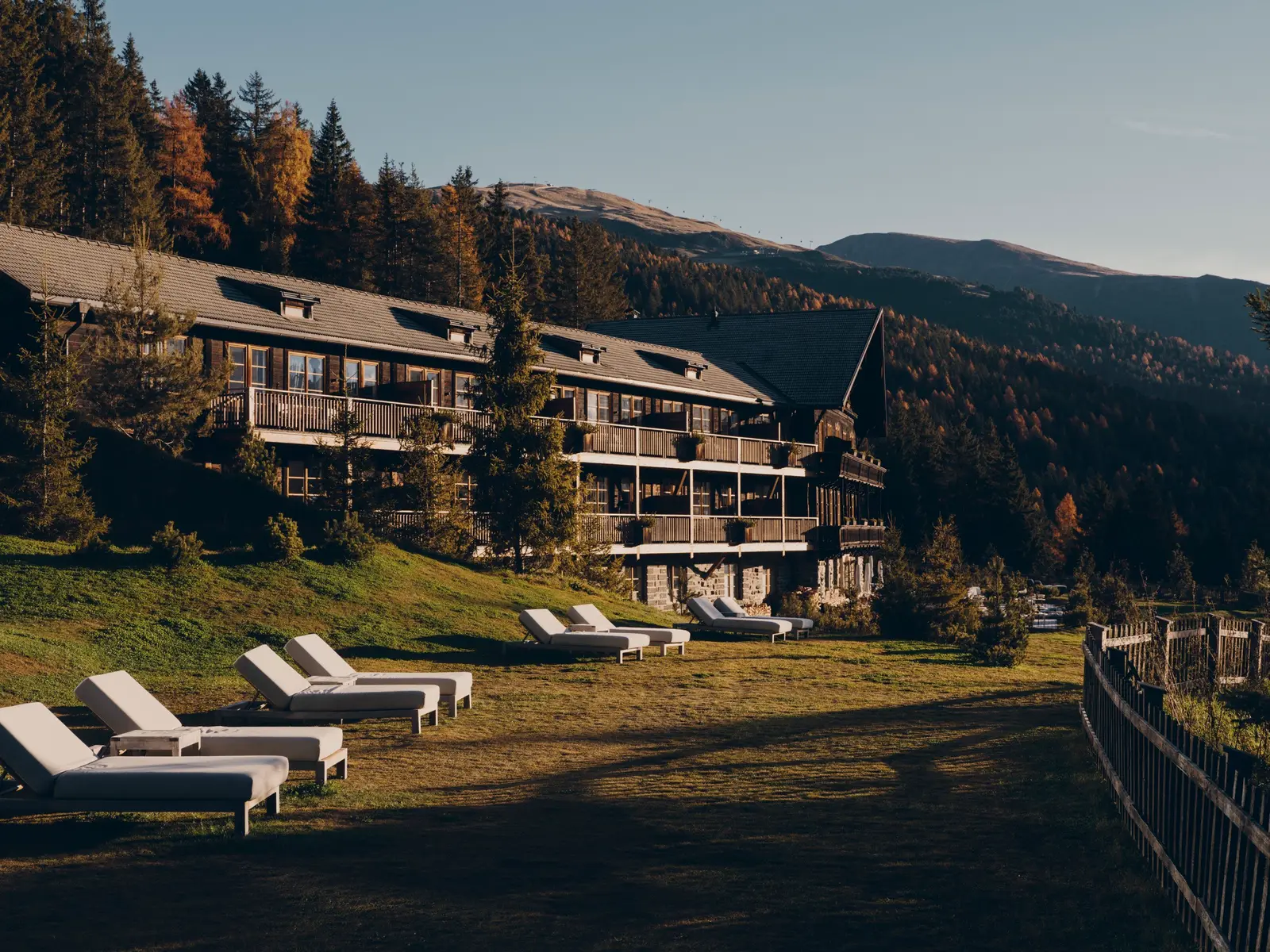The historic house of wood and stone with its balconies, loungers on the sloping lawn and the autumn forest behind.