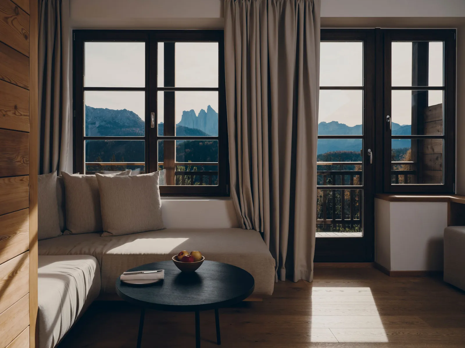 The living room of a Suite in the historic house: the corner sofa, the dark coffee table and the windows with the balcony onto the Dolomites.