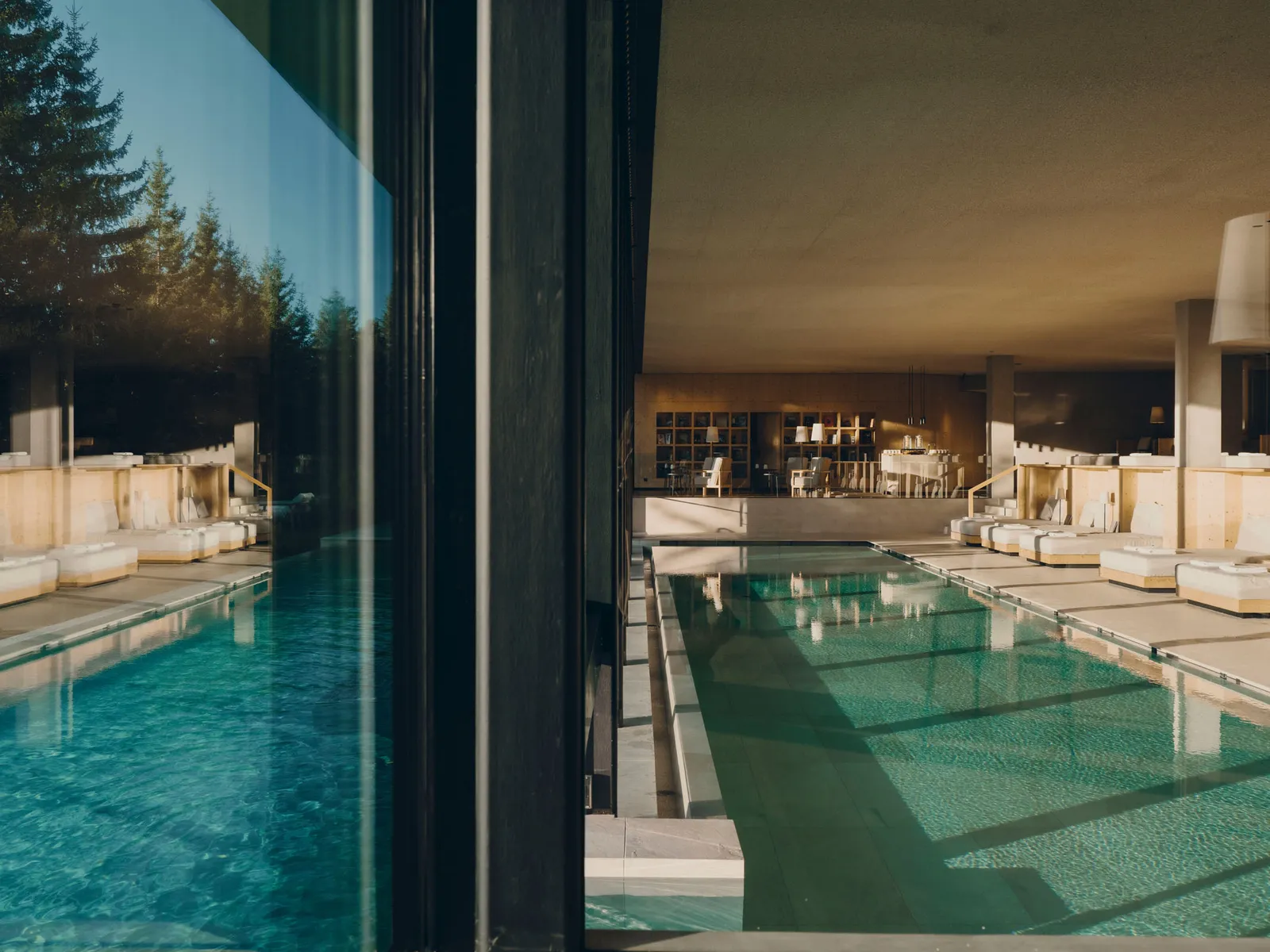The spa’s indoor pool, long and green between pale-wood daybeds, seen from outside through glass that reflects the firs.