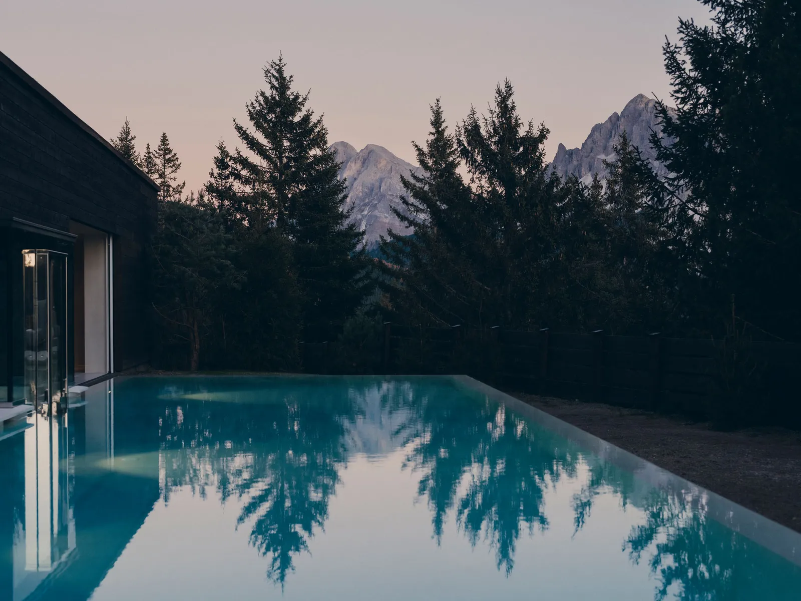 The Villa’s pool at dusk, the firs mirrored in turquoise water and 2 Dolomite peaks between the trees.
