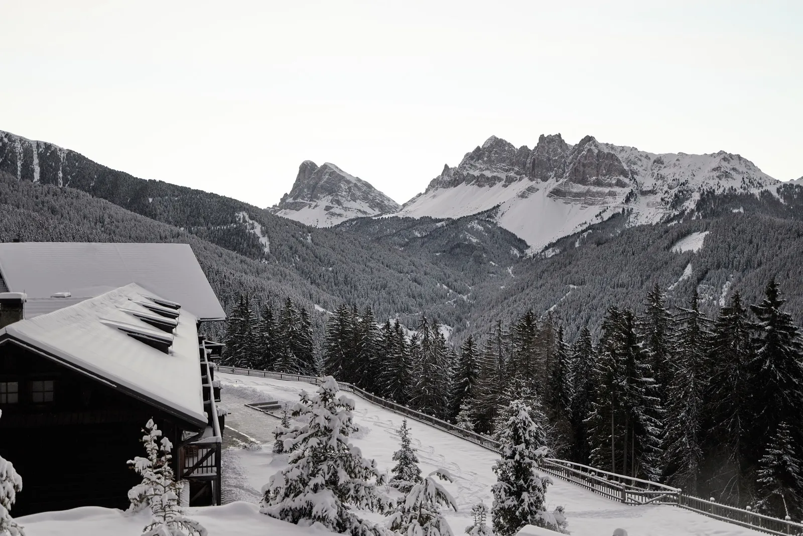 The snow-covered roof of the historic house, the white forest and, at the end of the valley, Sass de Putia and the Odle under a pale sky.