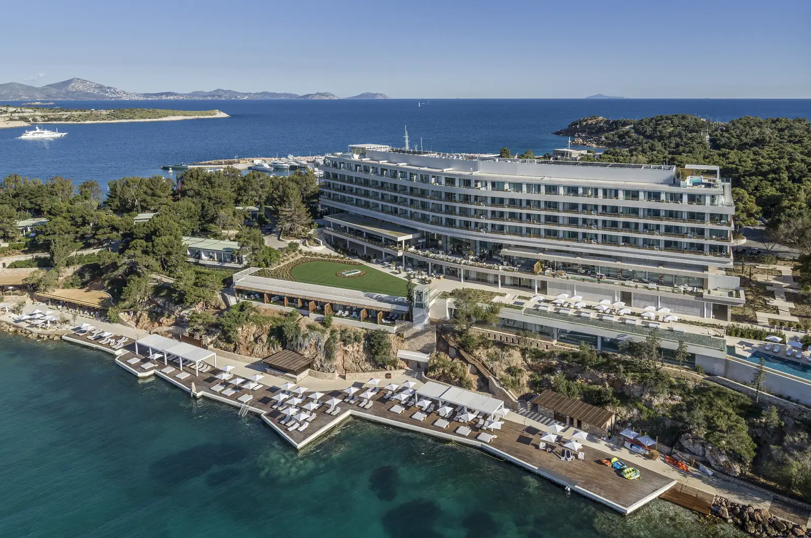 The Arion building from the air, long and white among the pines, with timber decks and loungers on the water and the marina behind.