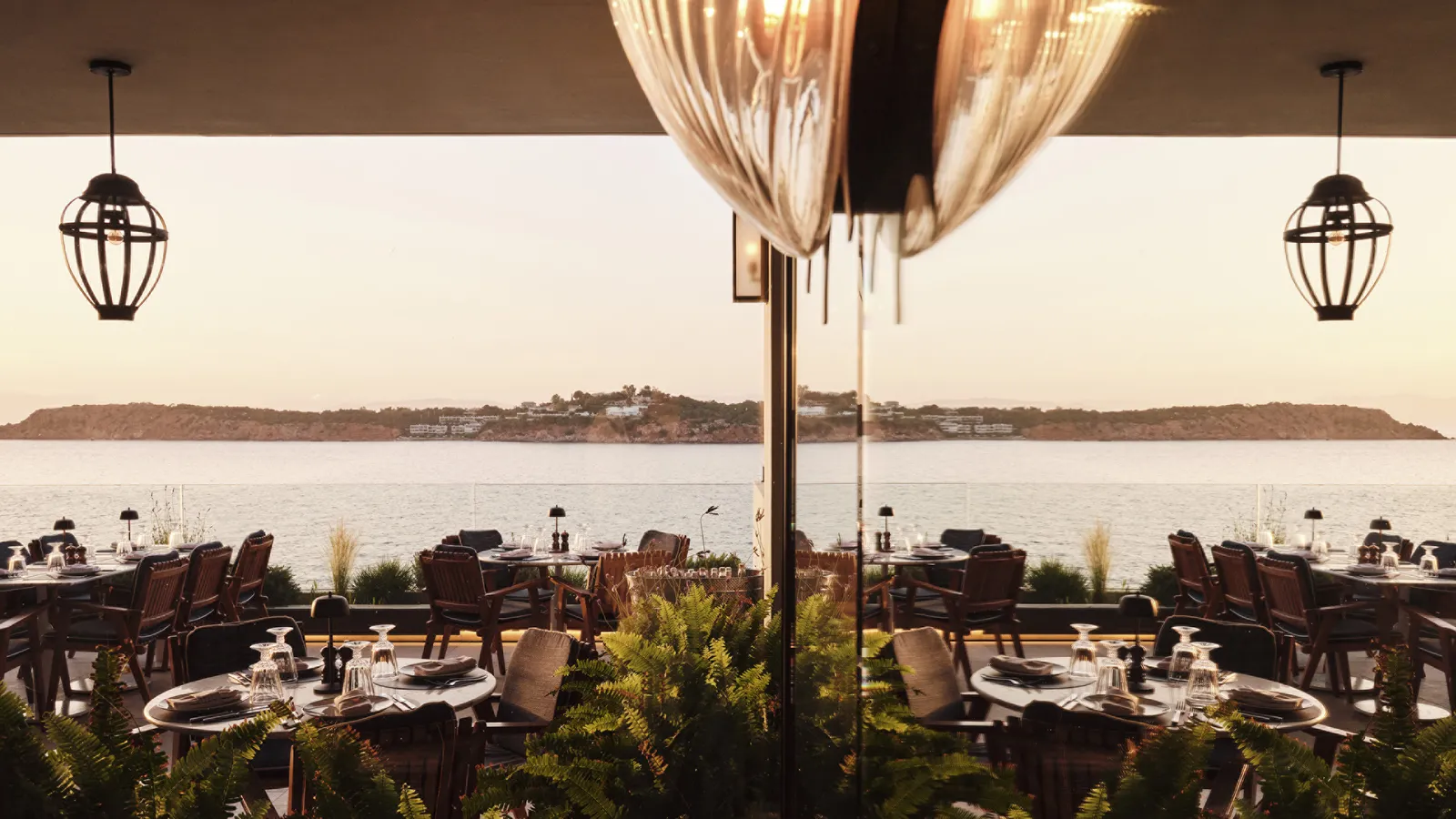 Mercato’s terrace at dusk, with laid tables, hanging lanterns and the coast opposite across the water.