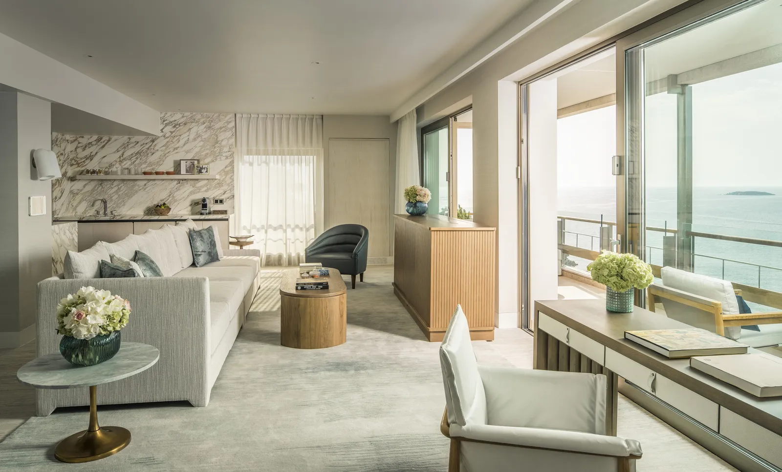 The living room of Arion’s Panoramic Sea-View Suite, with a long pale sofa, a marble bar corner and the corner balcony over the sea.