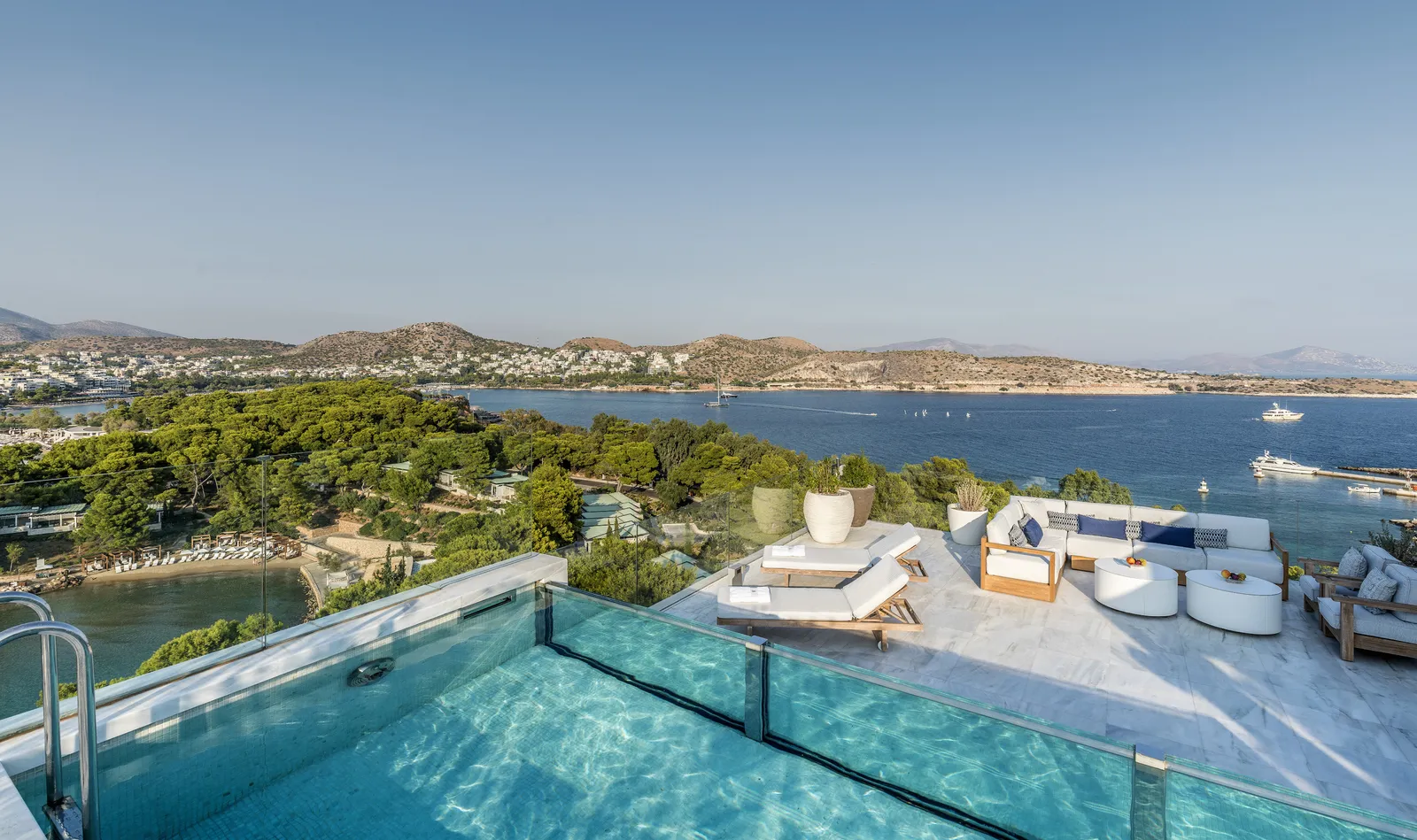 The rooftop pool of the Arion Riviera Suite, with outdoor sofas and, below, the pines, a cove and the houses of Vouliagmeni.