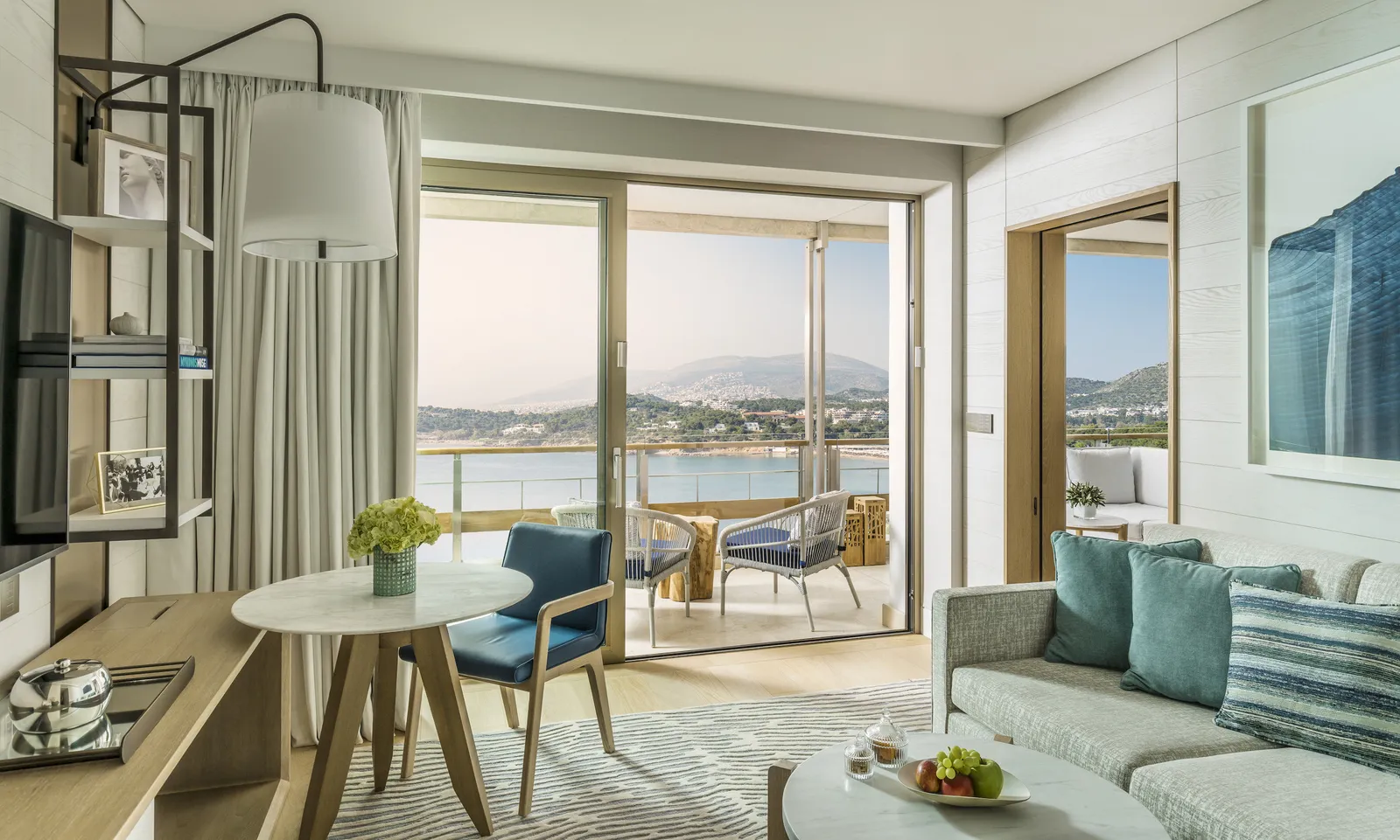 The sitting room of a sea-view Executive Suite, with an aqua sofa, a round table and the balcony over Vouliagmeni’s bay.