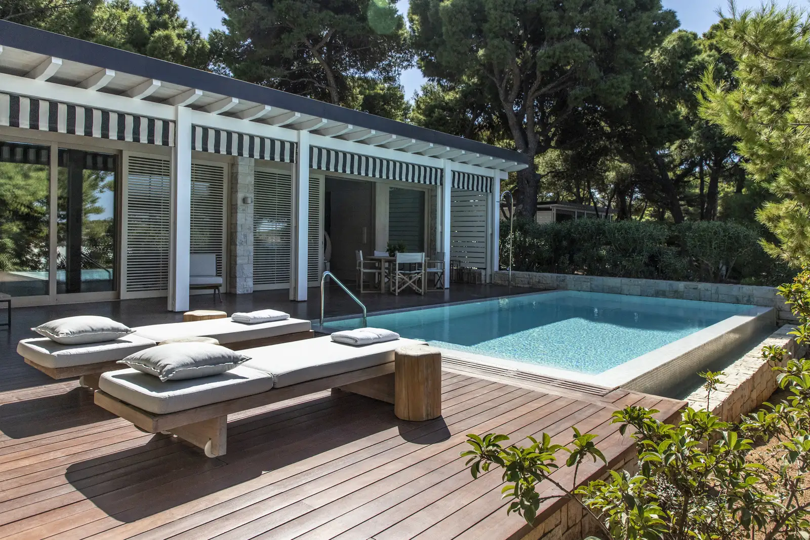 A garden-view Bungalow Suite from outside: the private pool, loungers on the timber deck and striped awnings among the pines.