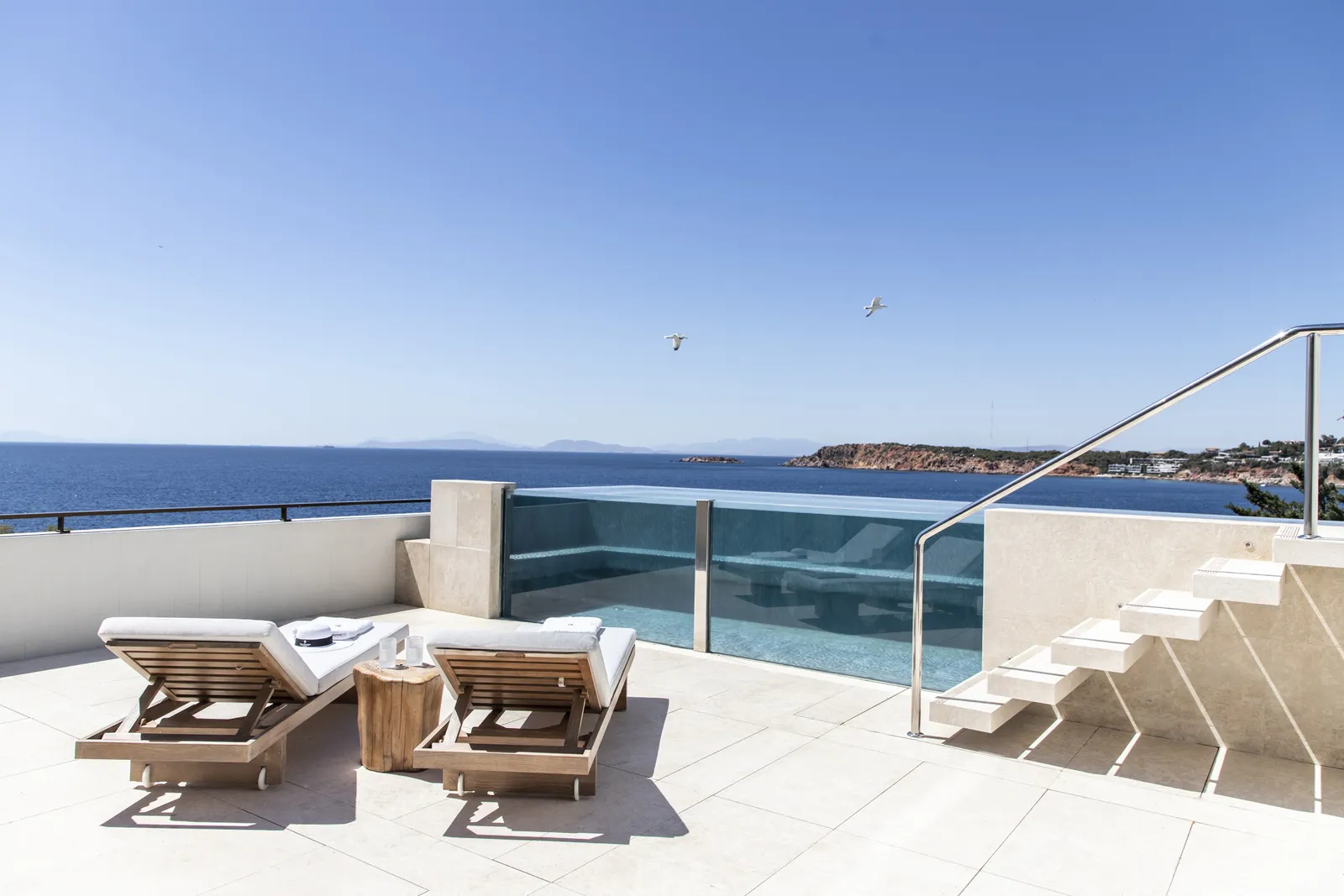 The terrace of the Nafsika Ambassador Suite, with 2 loungers, the glass pool reached by a white stair and the open sea.