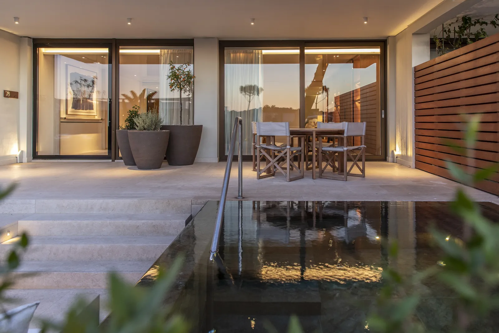 The terrace of a Nafsika Garden Suite at dusk, with its dark private pool, a dining table and lit glass doors.