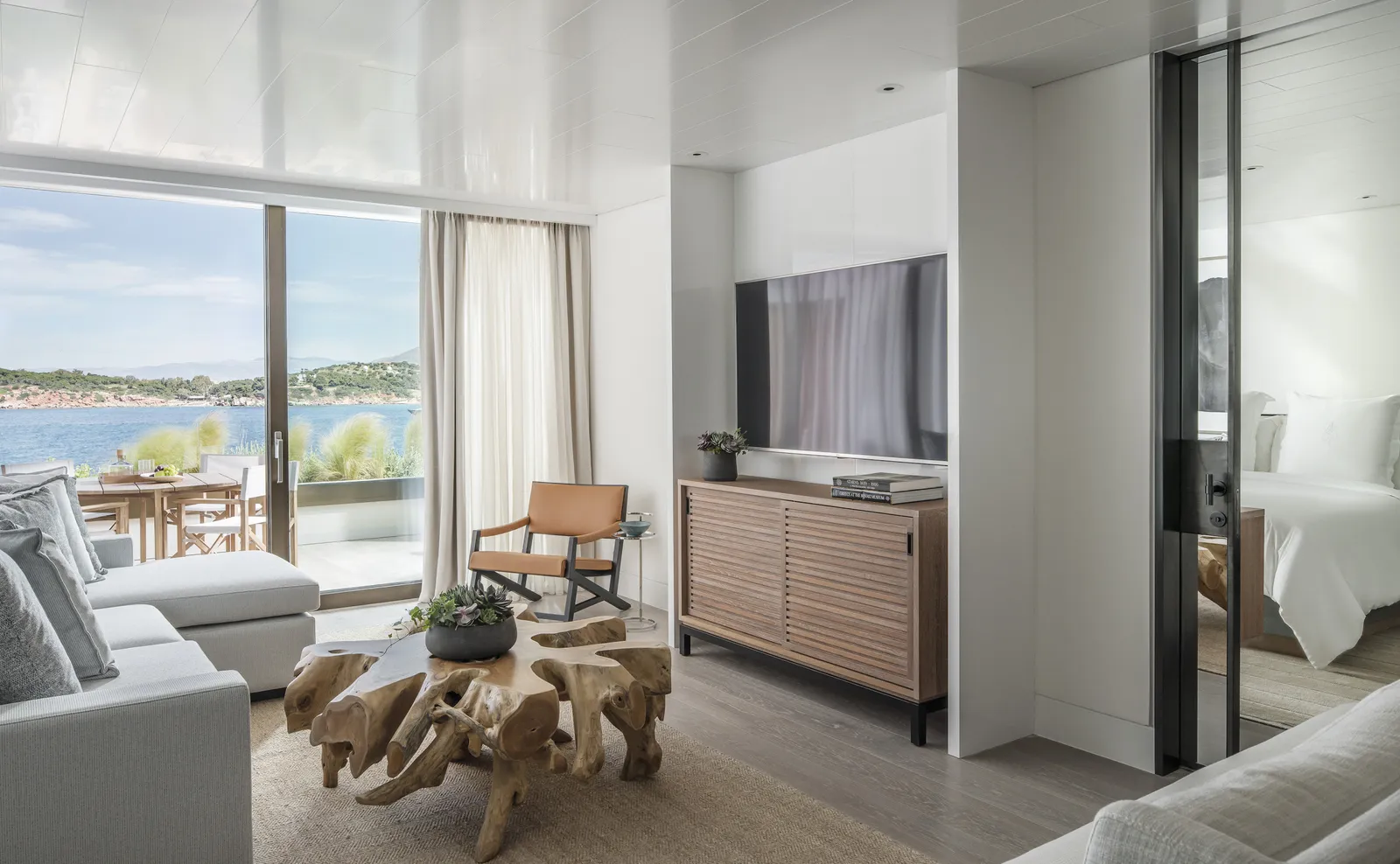 The living room of a Nafsika suite, with a coffee table cut from a tree root, a pale sofa and the furnished terrace over the bay.